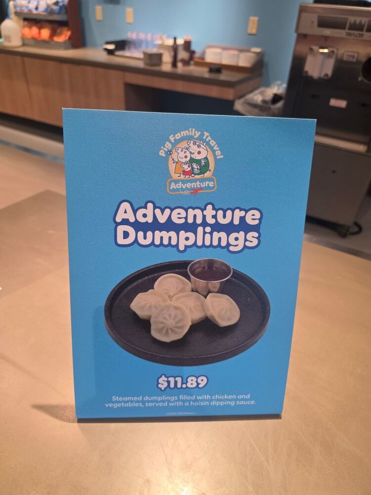 Blue sign/menu advertising 'Adventure Dumplings' with a photo of steamed dumplings on a black plate and dipping sauce; price $11.89.