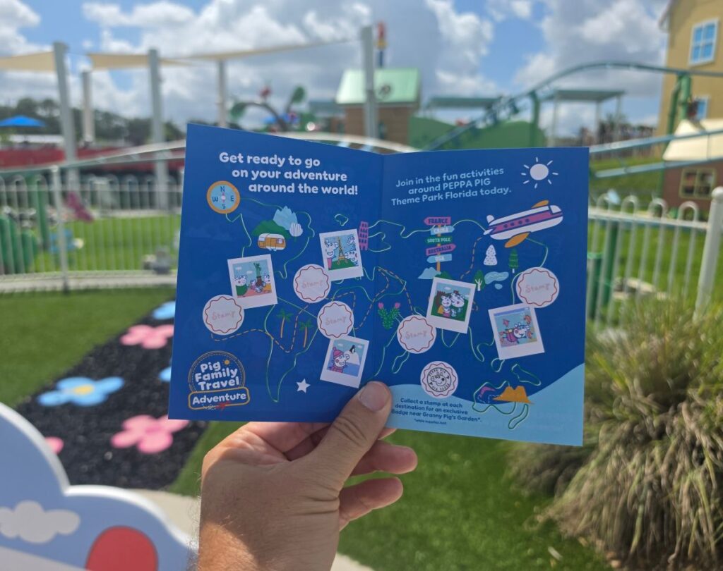 A person holding a blue travel map with stamps at a colorful outdoor theme park.