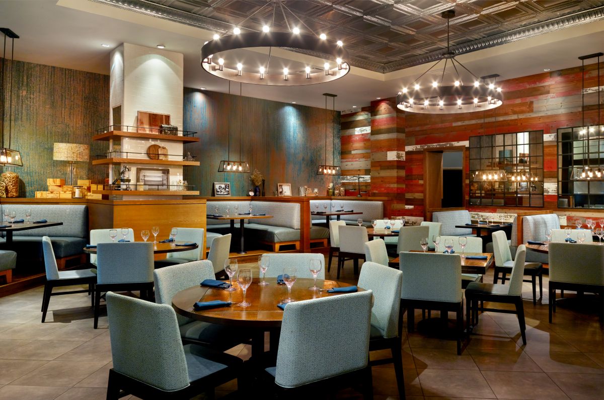 Modern restaurant dining room available with Orlando World Center Perks, featuring round wooden tables, light blue upholstered chairs, and circular chandeliers providing warm ambient light.
