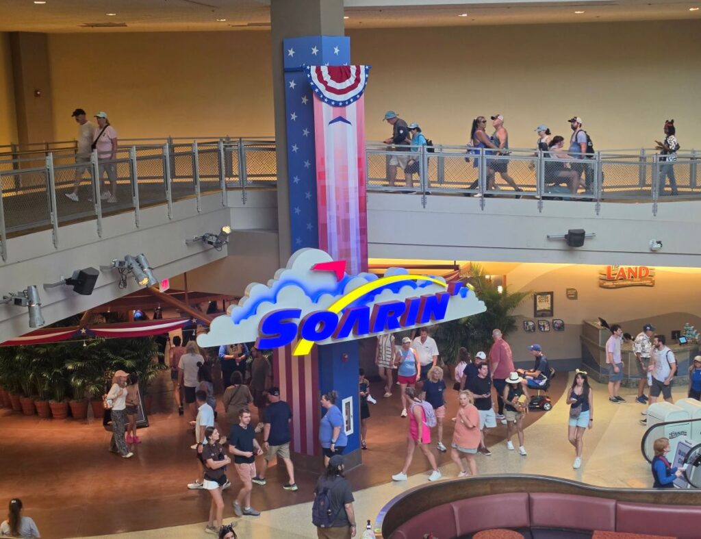 Busy indoor atrium with a large colorful sign that reads SOLRIN, people walking on ground level and a second-floor walkway with a patriotic bunting-adorned pillar nearby.