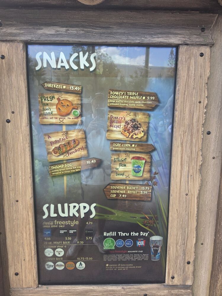 Wood-framed glass menu board listing snacks and slurps with prices, seen in a rustic setting.