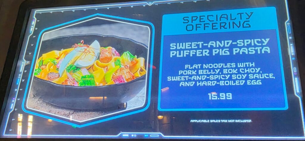 Digital menu board listing 'Sweet-and-Spicy Puffer Pig Pasta' with flat noodles, pork belly, bok choy, egg — $15.99 (specialty offering).