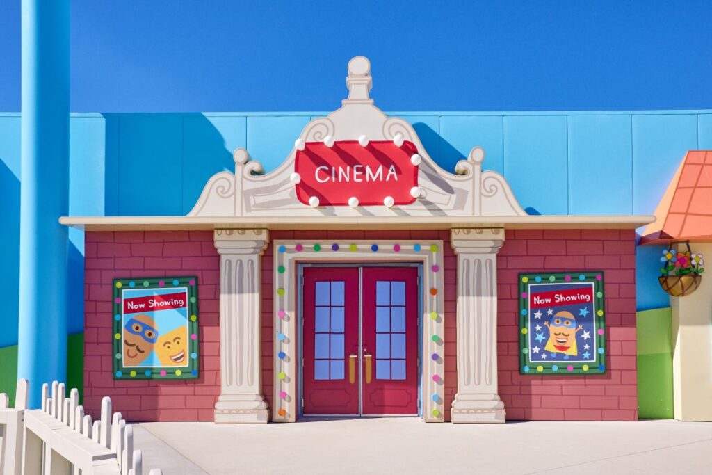 Colorful cartoon cinema building with bright pink walls, red doors, and a marquee reading CINEMA.