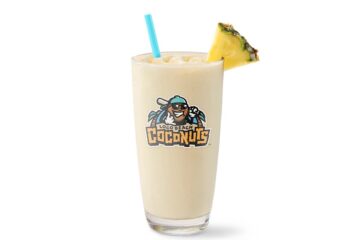 Tall glass of Loco Beach Colada Smoothie with pineapple–coconut smoothie with a blue straw and pineapple wedge, featuring the Loco Beach Coconuts logo on the cup.
