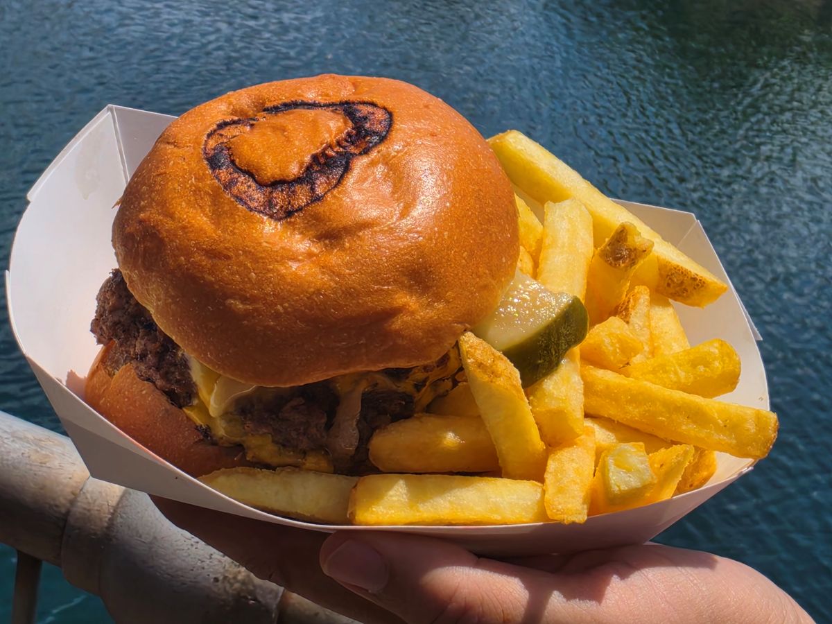 Burger with cheese and pickles in a bun, served with thick-cut fries on a white tray over blue water background for Richter's Burger Co Review