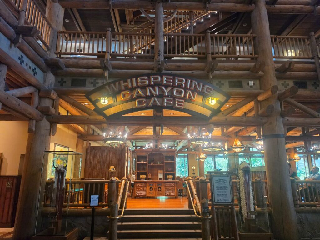 Rustic lodge interior with a large wooden sign reading 'Whispering Canyon Café' over a dining area.