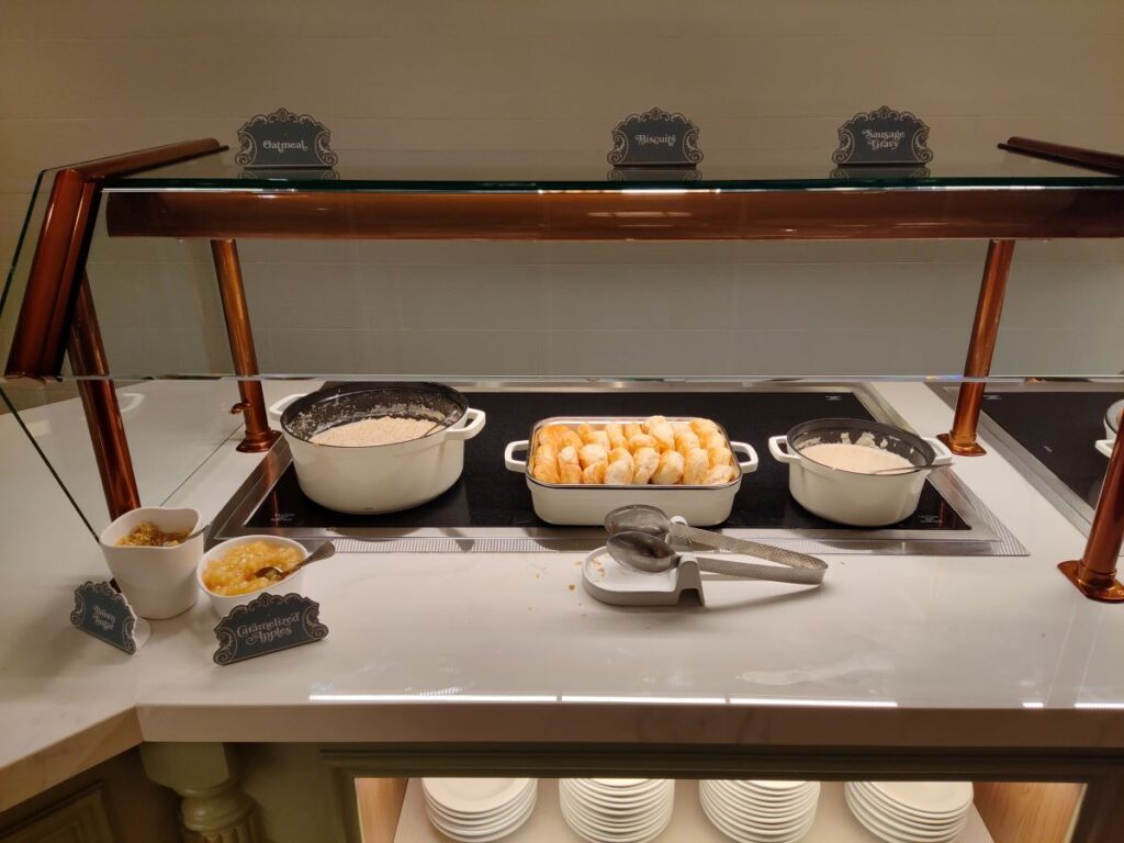 1900 Park Fare Breakfast buffet: warming pots for oatmeal and sausage gravy, a baking dish of croissants in the center, and labeled bowls of toppings on the side.