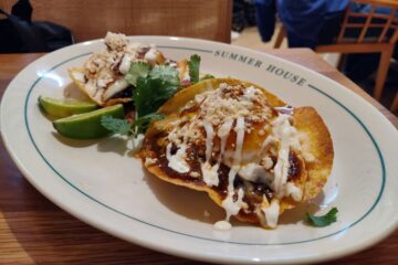 Plate with two crispy tortilla shells topped with cheese, crema, and crumbled toppings, garnished with cilantro; lime wedges on the side at Summer House restaurant.