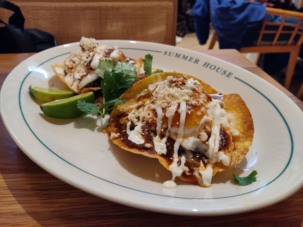 Plate with two crispy tortilla shells topped with cheese, crema, and crumbled toppings, garnished with cilantro; lime wedges on the side at Summer House restaurant.