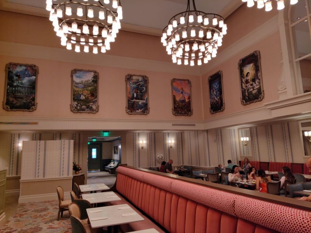1900 Park Fare breakfast Restaurant dining area with pink walls, ornate framed paintings, and large circular chandeliers above a red upholstered banquette.