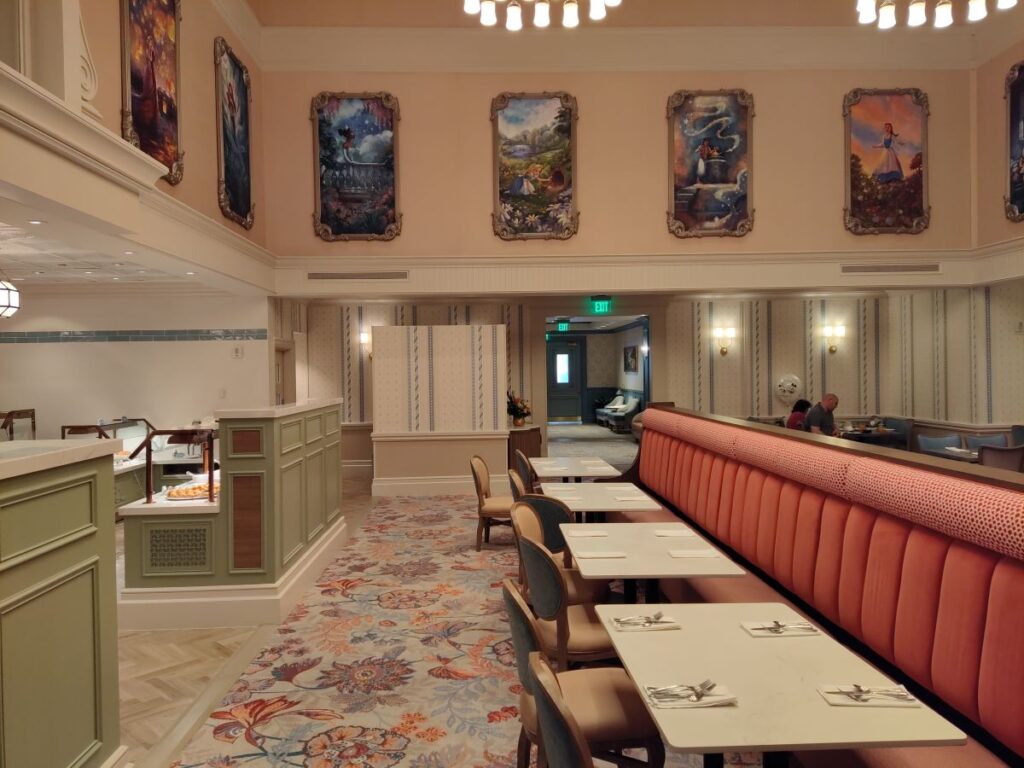 Elegant restaurant dining area with a long pink banquette, white tables set for two, and pastel walls adorned with framed paintings.