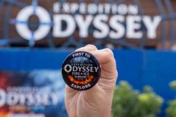 Hand holding a round badge that says Expedition Odyssey Fire & Ice, SeaWorld Orlando, with 'Explore' at the bottom and a fiery design edge.