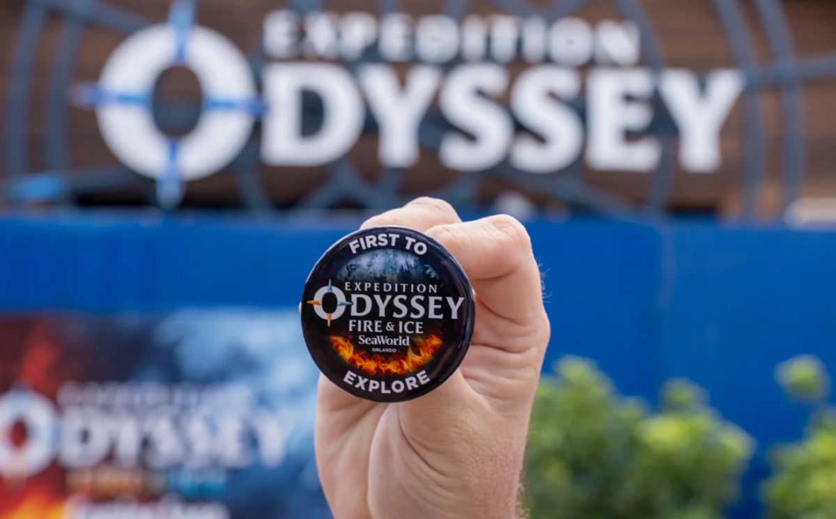 Hand holding a round badge that says Expedition Odyssey Fire & Ice, SeaWorld Orlando, with 'Explore' at the bottom and a fiery design edge.