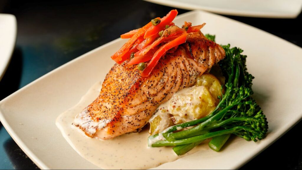Seared salmon fillet with black pepper crust, topped with carrot ribbons and capers, on a bed of creamy potato-herb sauce and broccolini on the side.