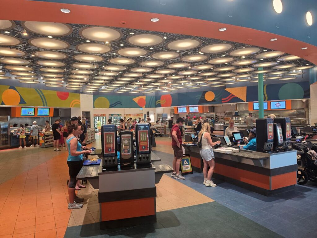 Bright, colorful cafeteria with self-serve stations and customers queuing at counters.