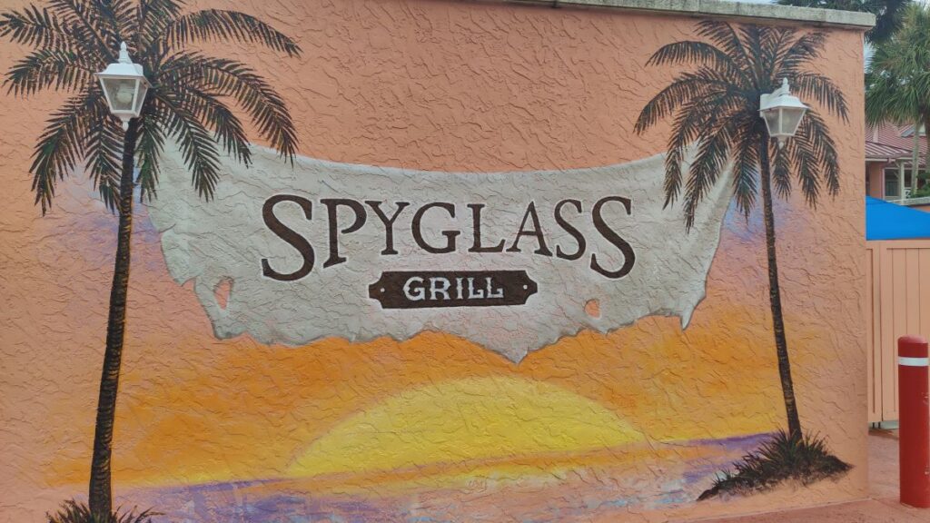 Mural on an orange textured wall with two palm trees and a sunset behind a stone banner that reads 'SPYGLASS GRILL'.