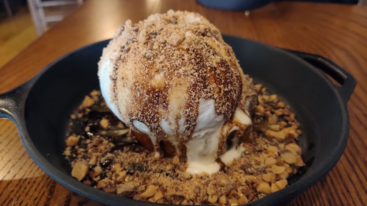 Skillet dessert with a large scoop of vanilla ice cream, caramel drizzle, and a crumbly nutty crust around the base in a black cast-iron pan