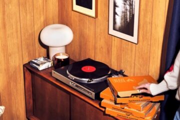 Turntable on a wood-paneled cabinet with a red-centered vinyl, a lamp, candle, and a stack of orange boxes nearby. IMage is for Blaze Pizza Delivery Offer
