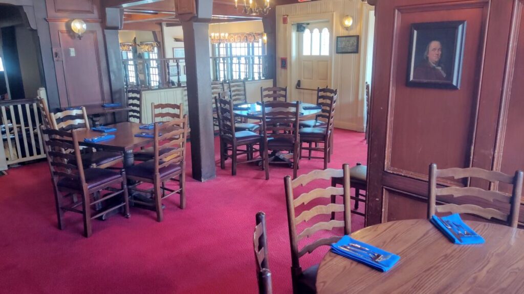 Cozy dining room with wooden tables and tall chairs on a red carpet, blue napkins set at each place.