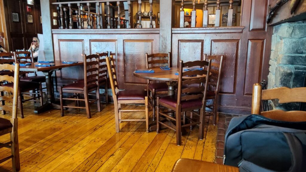 Cozy restaurant interior with dark wood tables and chairs, blue napkins, and warm lighting.