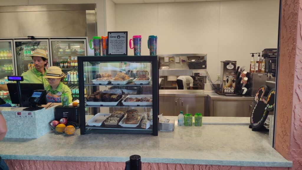 Bakery counter with a glass display case of pastries and two staff in green uniforms behind the counter.