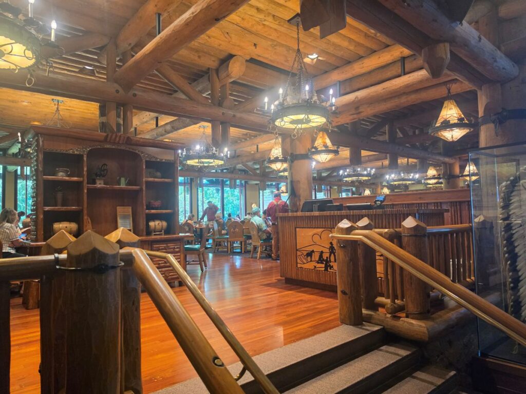 Rustic lodge-style restaurant with exposed wooden beams, warm chandeliers, and diners at tables.