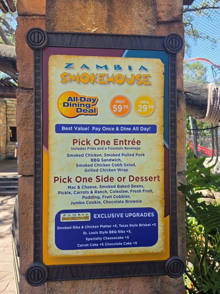 Sign for Zambia Smokehouse with all-day dining deal and menu items including entrees and sides and prices for adults and children (outdoor setting).