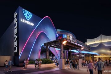 An artist's concept rendering of the Level 99 Disney Springs exterior at night, showing a modern, dark building facade illuminated with bright neon blue and pink geometric arches. The words "LEVEL 99" are displayed in glowing white text, running vertically down the side and horizontally beneath a triangle logo. People are depicted walking along the illuminated outdoor pathway and sitting on a low stone wall beneath an industrial-style awning.