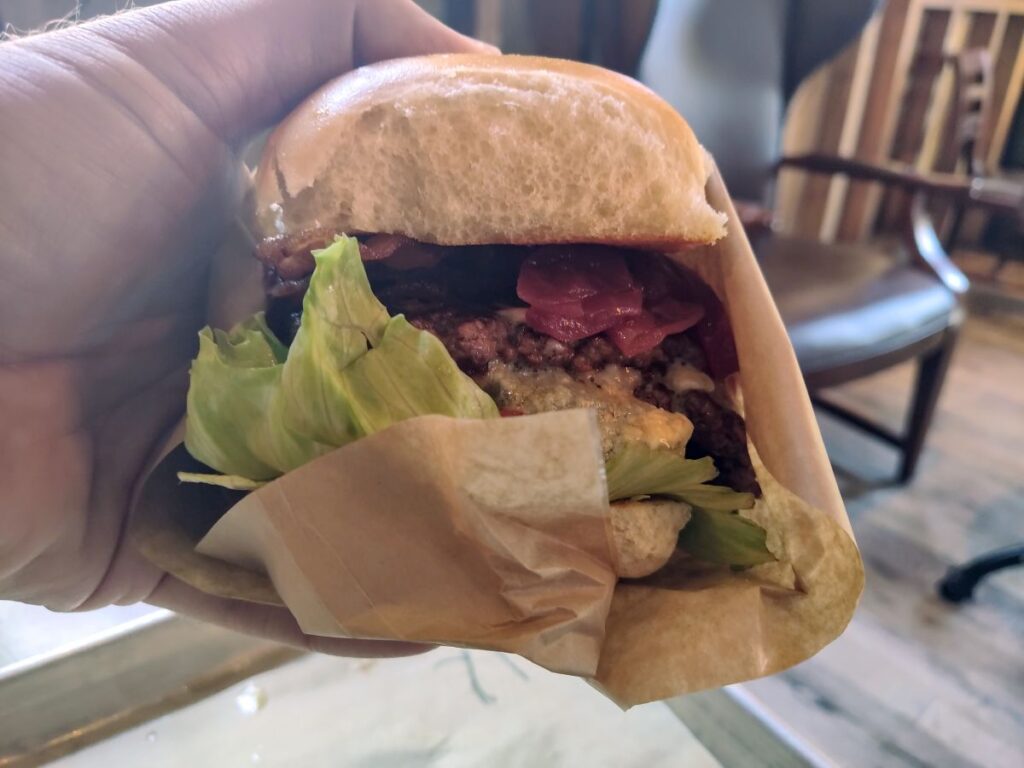 A hand holding the Bacon and Blue Burger at D-Luxe Burger Disney Springs