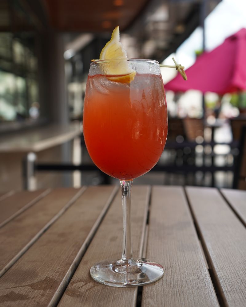 A refreshing berry lemonade Aperol spritz cocktail in a wine glass, garnished with a fresh lemon wedge on an outdoor patio table