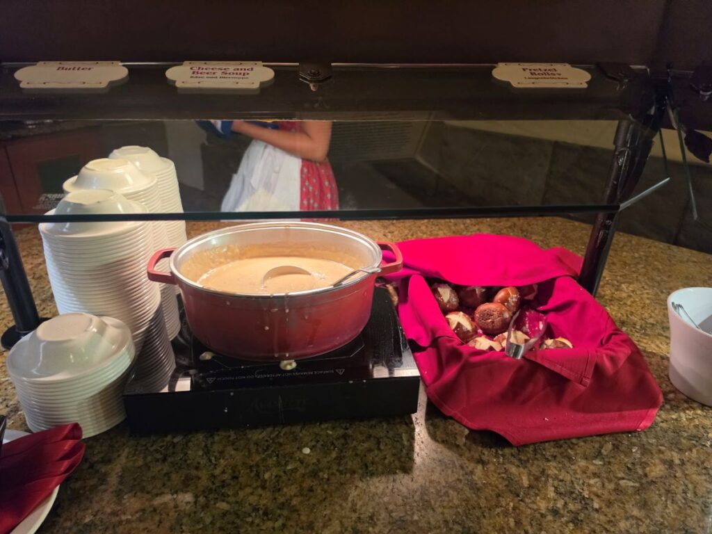 Biergarten Epcot review - photo on a buffet line with a large container of beer and cheese soup next to several pretzel rolls
