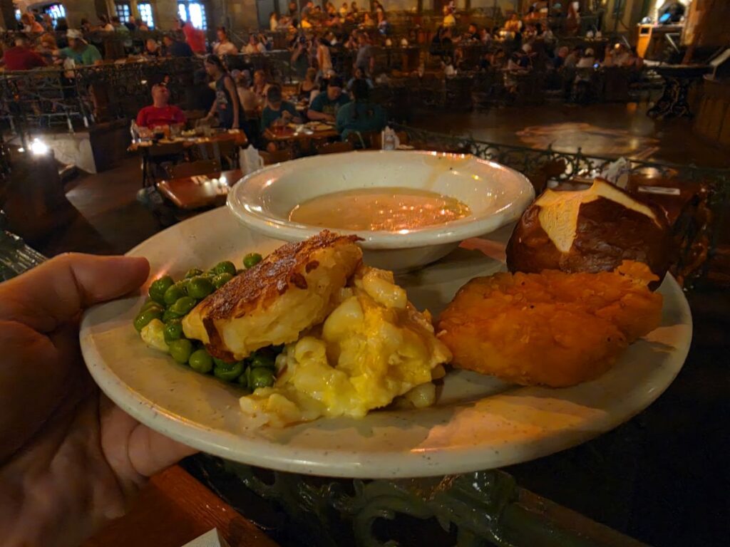Biergarten Epcot review- plate shown with beer-and-cheese soup, a pretzel roll, potato pancakes, and other German food