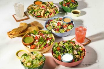 A variety of fresh Blaze Pizza entree salads topped with colorful vegetables, chicken, and dressings, served alongside garlic breadsticks and cold drinks for a summer meal.