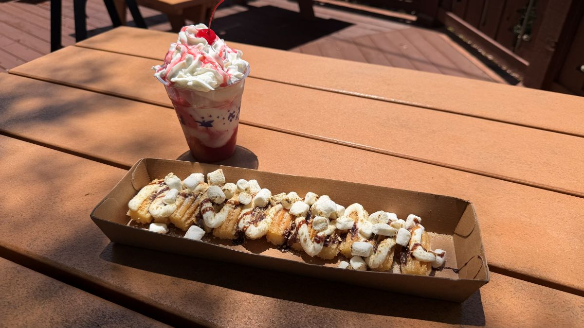 Blizzard Beach treats overhead view of a S'mores Churro tray loaded with mini marshmallows and chocolate drizzle alongside a layered strawberry shortcake dessert.