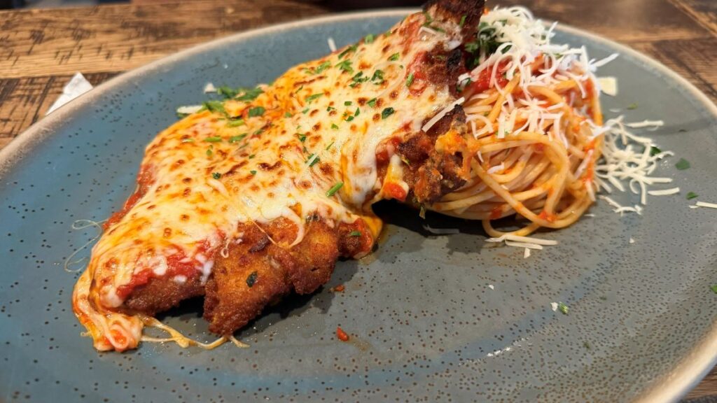 A large breaded and fried Chicken Parmesan cutlet smothered in melted mozzarella cheese and marinara sauce, served alongside a twirled portion of spaghetti topped with shredded cheese at Terralina Crafted Italian.