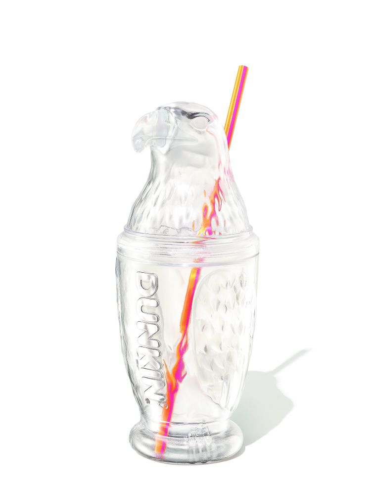A patriotic clear plastic collectible cup shaped like an American eagle, part of the Dunkin Fourth of July merchandise collection. The cup features a detailed eagle head as the lid and embossed "DUNKIN'" branding along the side, with a vibrant pink, orange, and yellow striped reusable straw inserted through the top.