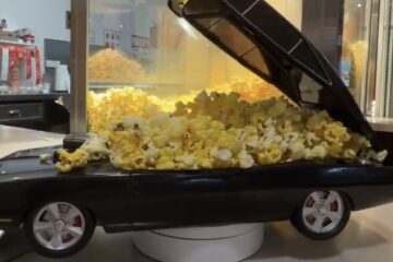 A close-up shot of official Fast & Furious merch at a Cinemark concession stand, showing the black Dodge Charger collectible popcorn bucket with its top opened up and filled to the brim with fresh movie theater popcorn.