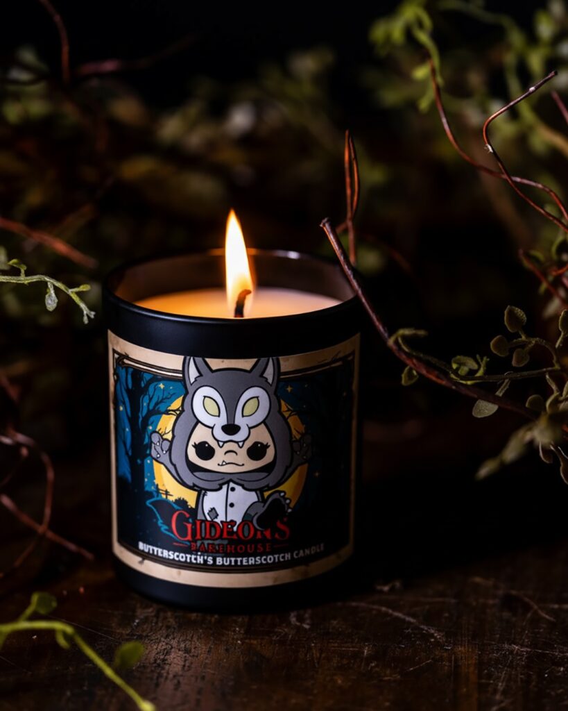 Lit candle in a dark glass container with a cartoon wolf mascot and the text Gideon’s Bakehouse on the label.