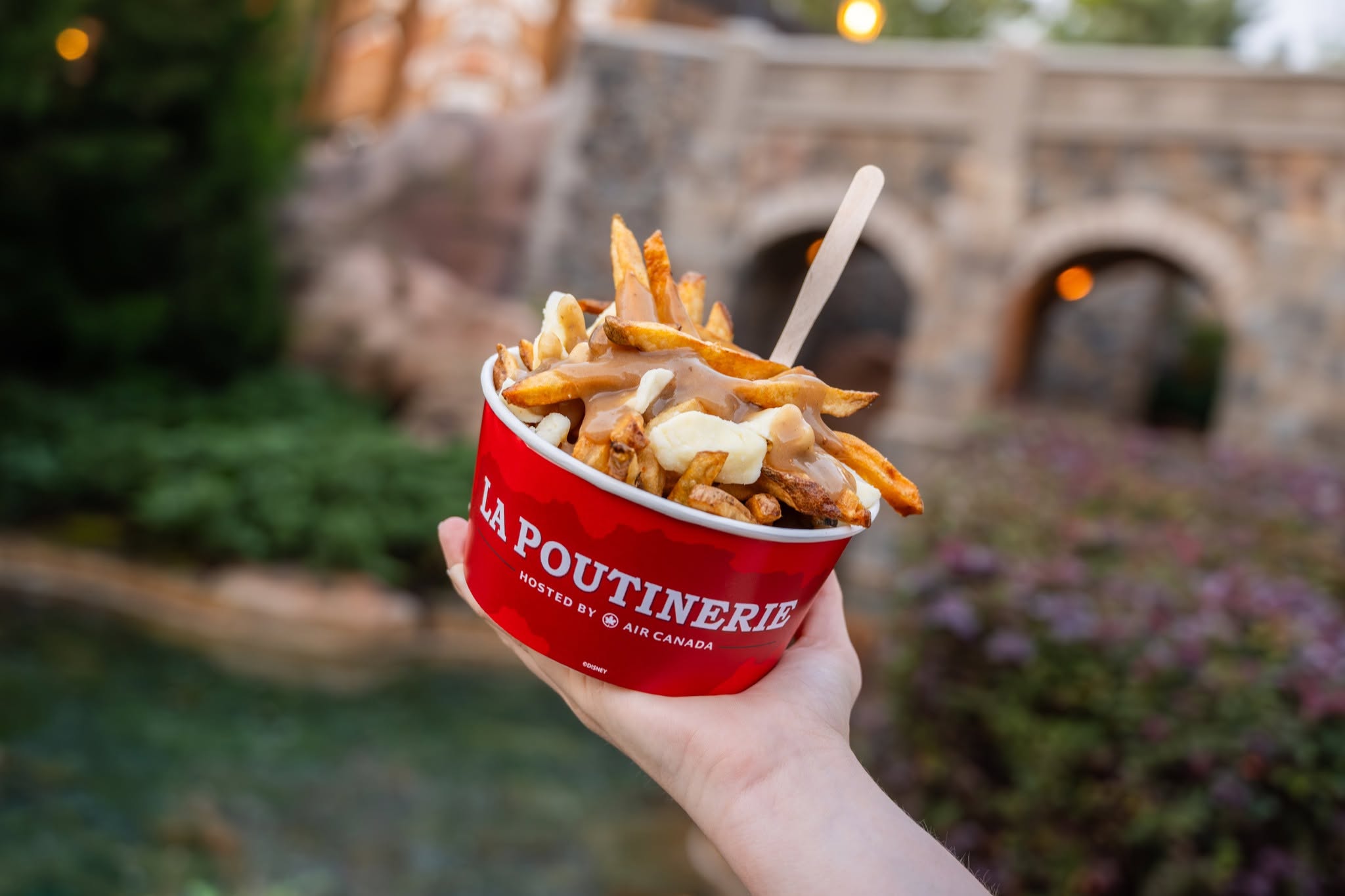 La Poutinerie Epcot poutine show in front of a Canadian background at Epcot