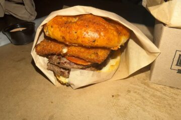 View of Pepperoni Pizza Burger wrapped in paper with bread, burger patties, and fried mozzarella shown