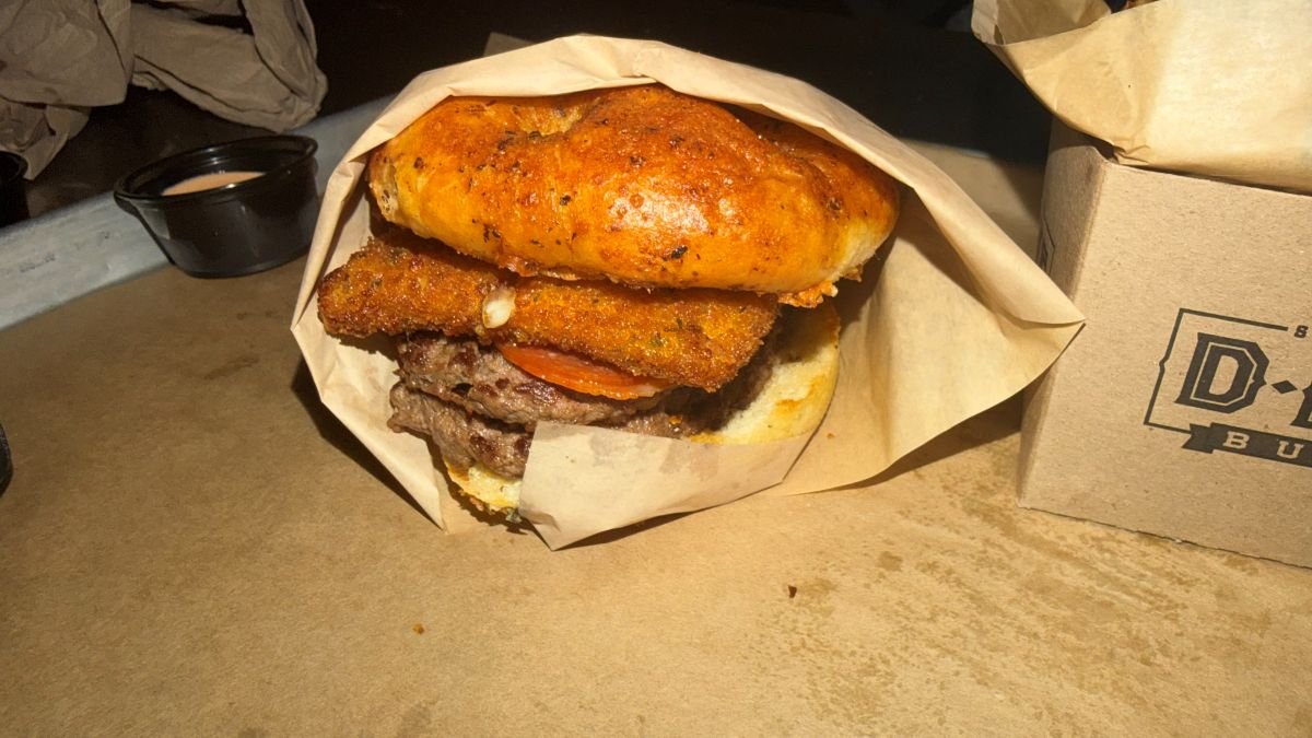 View of Pepperoni Pizza Burger wrapped in paper with bread, burger patties, and fried mozzarella shown