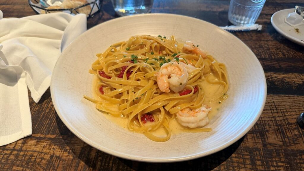 A white bowl filled with a generous serving of shrimp fettuccine pasta tossed in a light, creamy sauce with sun-dried tomatoes and sprinkled with fresh herbs at Terralina Crafted Italian.