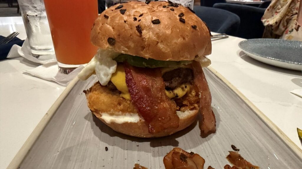 Steakhouse 71 Breakfast Burger shown on a white plate. it features bacon, hashbrowns, avocado, and a fried egg