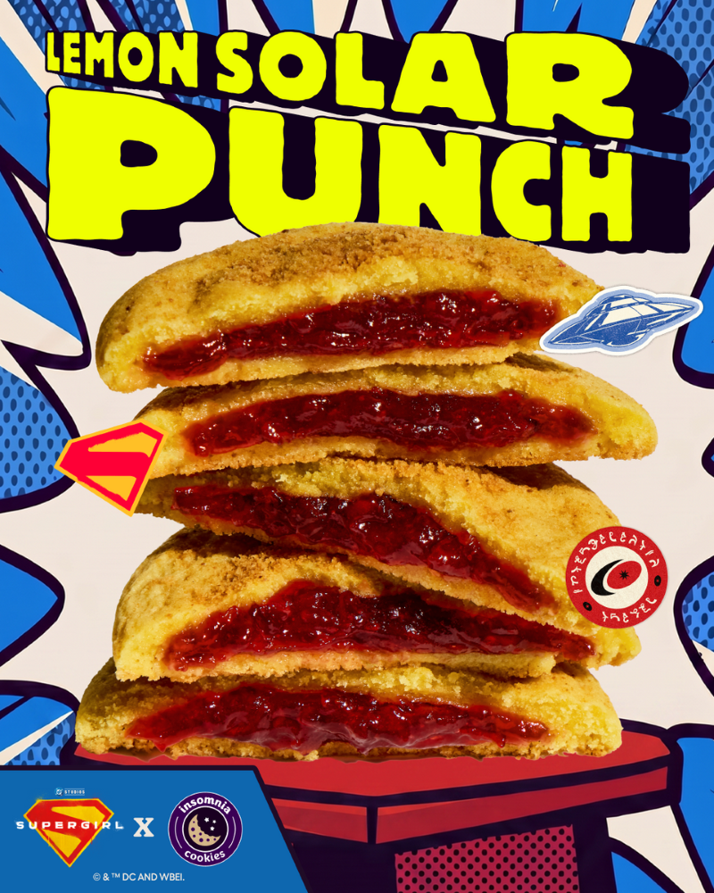 A vertical stack of five halved Lemon Solar Punch cookies from Insomnia Cookies against a comic book-style background. The golden cookies are sliced open to reveal a bright red strawberry jam filling. The text "LEMON SOLAR PUNCH" is written in large yellow comic font at the top, with a collaborative Supergirl and Insomnia Cookies logo at the bottom.
