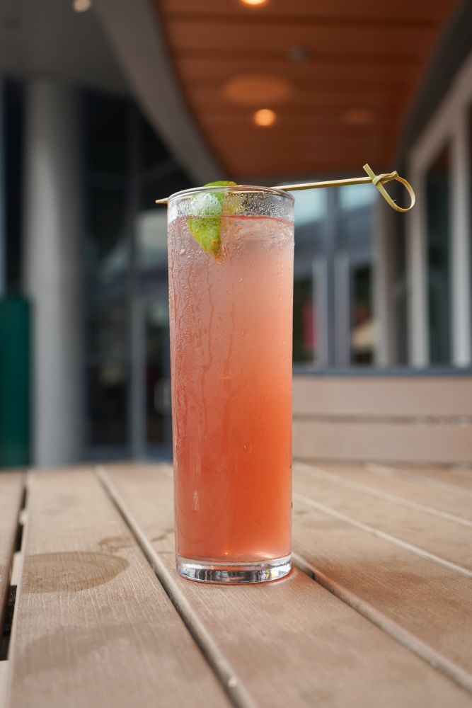 A tall, iced Transfusion cocktail garnished with a lime wedge on a wooden outdoor dining table