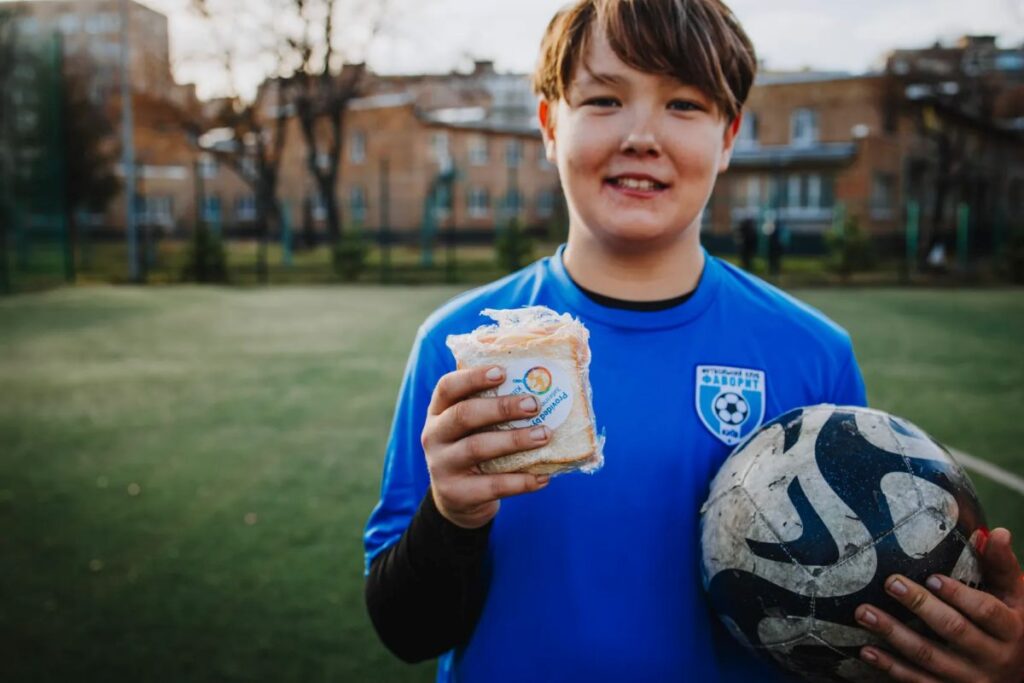 World Cup Food Giveaway image showing a child with a soccer ball and a handheld food item from the World Central Kitchen.