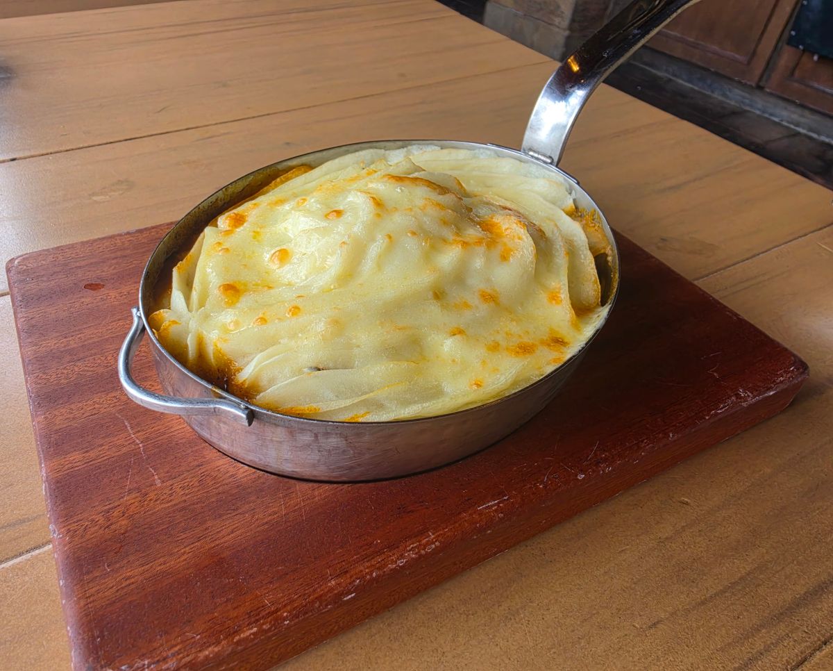 Cottage Pie shown in an oval metal pan with a handle. The top consists of creamy-looking potatoes for a Rose & Crown Review