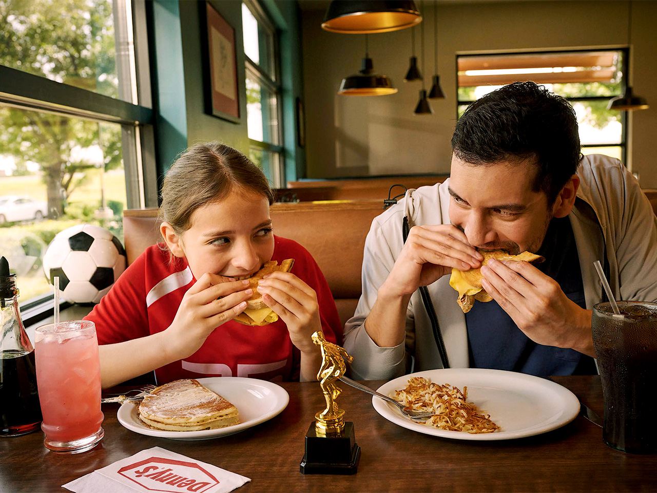 father and daughter eating at Denny's with a soccer ball off to the side of their table