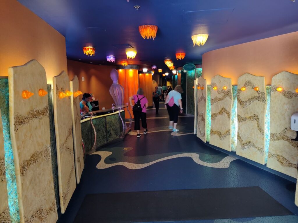 The underwater-themed entrance hallway of the restaurant, featuring wavy floor patterns, sandy textured wall panels, and glowing jellyfish ceiling lights ahead of the Coral Reef Closing.