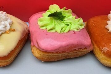 Three frosted square donuts in a red box: left with white glaze, whipped cream, and cherry; middle pink glaze with green rosette; right orange glaze with whipped cream and candied orange for an Everglazed Disney Springs review
